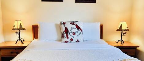 A neatly made bed with white linens, two wall-mounted lamps, and two framed floral pictures.