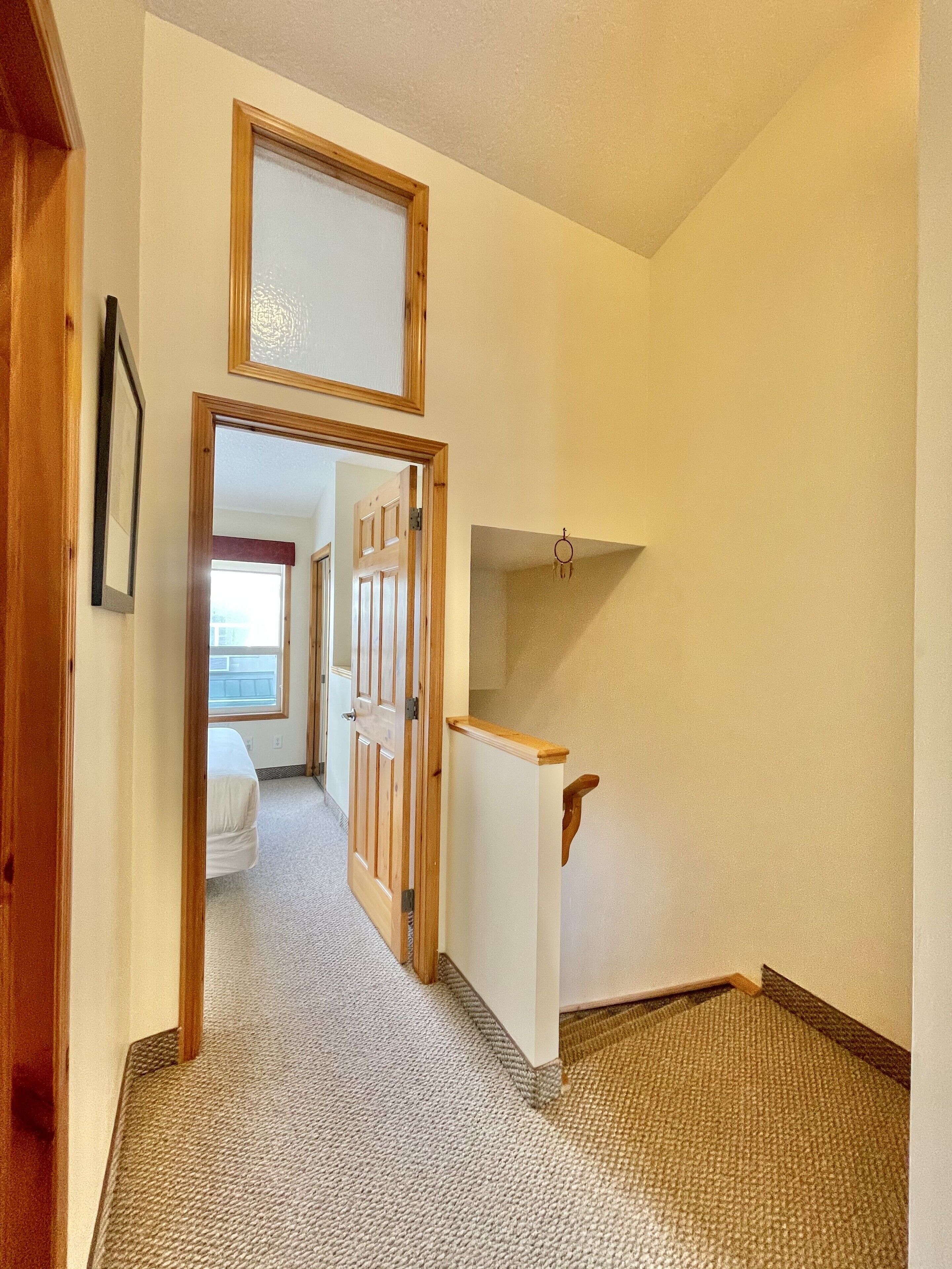 A hallway with a carpeted floor, wooden doors, and a white wall with a picture frame.