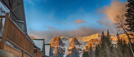 A mountain lodge with a wooden balcony overlooking a snowy mountain range.