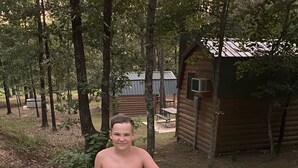 A hot tub with three people, surrounded by trees and a wooden cabin.