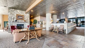A spacious lobby with a stone fireplace, a wooden coffee table, and comfortable seating. - Sixth-Floor Condo w/ a Shared Hot Tub, Pool, Free WiFi, & an Electric Fireplace (Sugar Mountain)