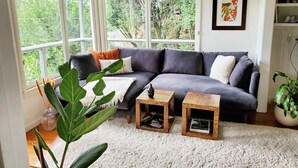 Ein gemütliches Wohnzimmer mit einer grauen Couch, zwei Holztischen und einer großen Pflanze.