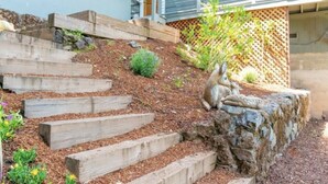 Holzstufen führen zu einer Steinmauer, am Fuße befindet sich ein kleiner Garten.