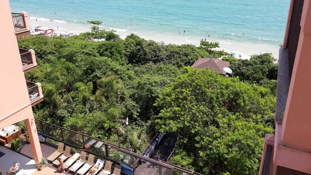 Un balcone con vista sulla spiaggia, vegetazione lussureggiante e cielo sereno.