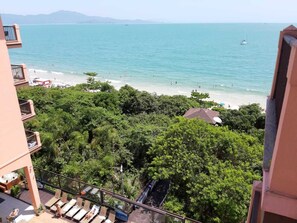 Un balcón con vista a una playa, follaje exuberante y cielo despejado.