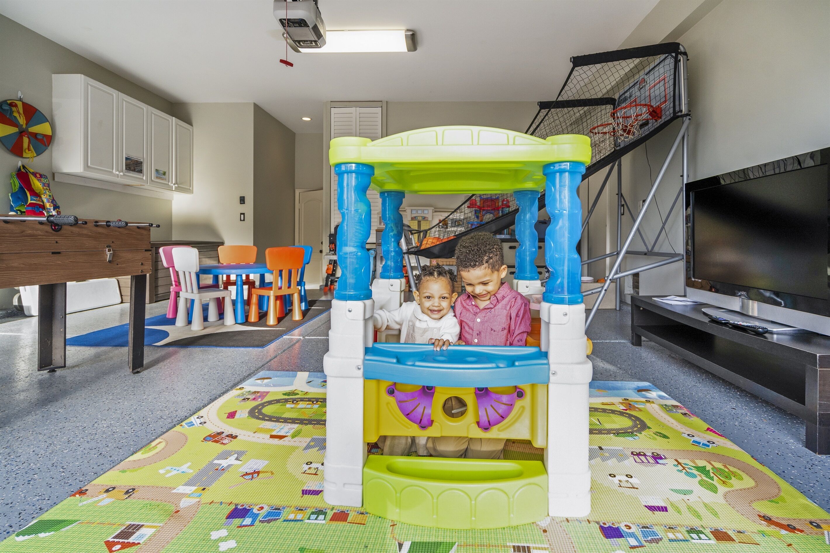 Un espace de jeux avec un toboggan et une structure d’escalade, un téléviseur et un coin repas avec des chaises et une table.