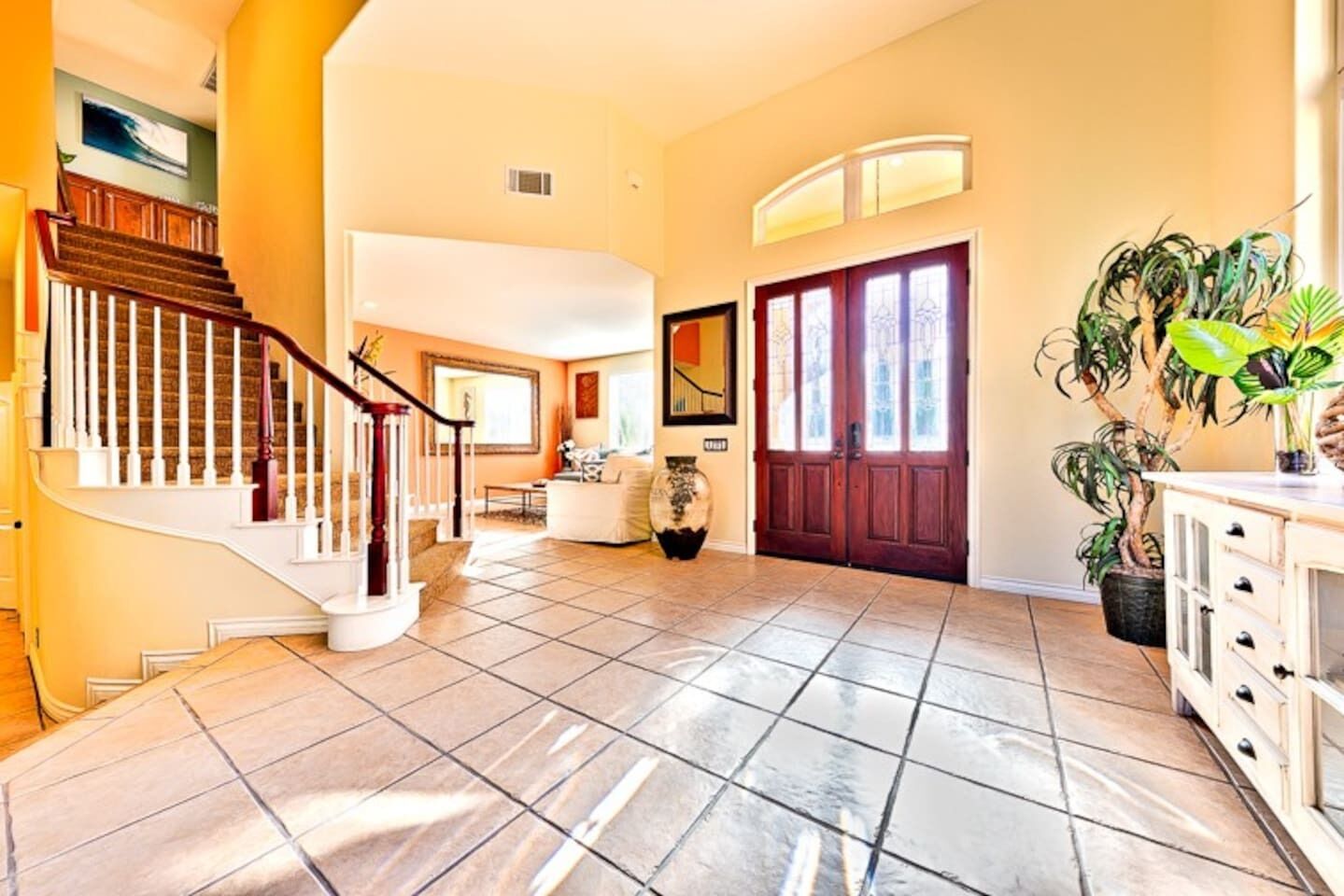A spacious foyer with a tiled floor, a wooden staircase, a large door, and a potted plant.