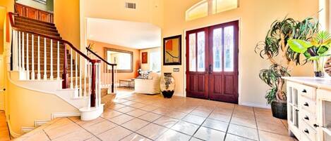 A spacious foyer with a tiled floor, a wooden staircase, a large door, and a potted plant.