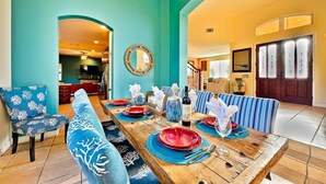 A dining area with a wooden table set for four, blue upholstered chairs, and a large mirror on the teal wall. - Casa Surfside-Walk 2 Beach, Spa, Close to Legoland (Carlsbad)