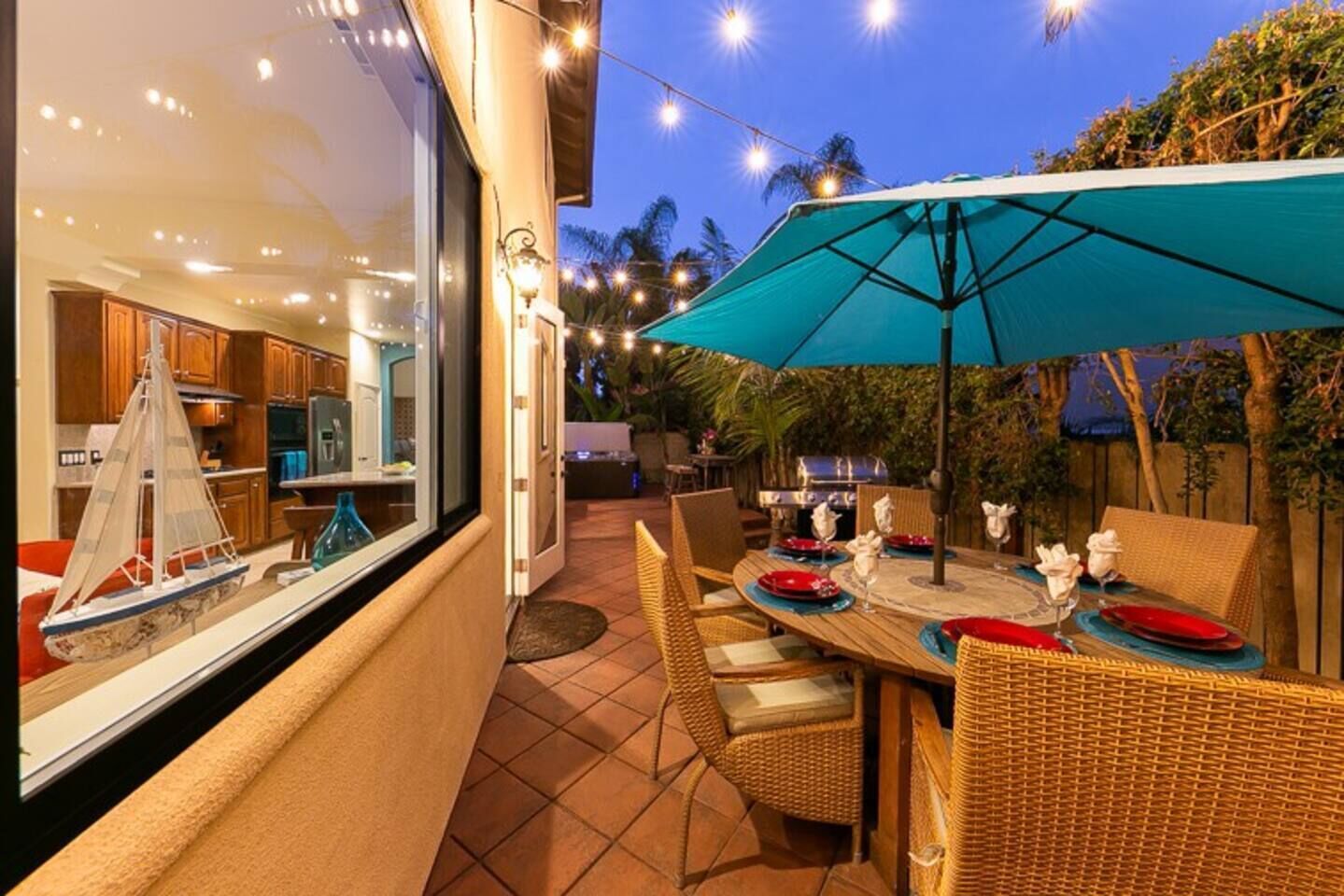 Un patio con mesa lista para comer, un paraguas grande y un modelo de velero en la ventana.