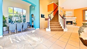 A spacious living area with a staircase, a fireplace, and a dining area with a view of the outdoors. - Casa Surfside-Walk 2 Beach, Spa, Close to Legoland (Carlsbad)
