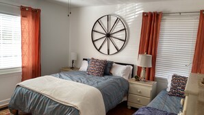 A bedroom with two beds, a large wall clock, and a window with curtains.