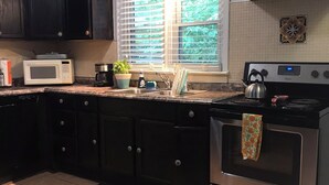 A kitchen with dark cabinets, a microwave, a stove, and a window with blinds.