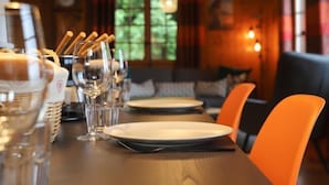 Ambiente de restaurante com mesa de madeira posta para refeição, incluindo pratos, copos e talheres.