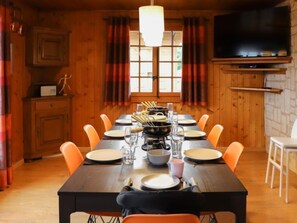 Un coin repas avec une longue table dressée pour le repas, des murs en bois, un téléviseur et une fenêtre avec des rideaux.