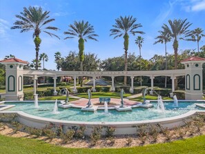 A fountain surrounded by palm trees and a white archway with the text "Emerald Island". - Fall Retreat near Disney, Perfect for families (Kissimmee)