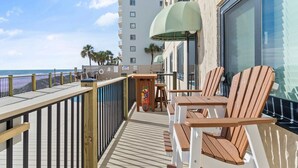 Une terrasse dotée de chaises et de tables en bois, offrant une vue sur une plage et un immeuble imposant.