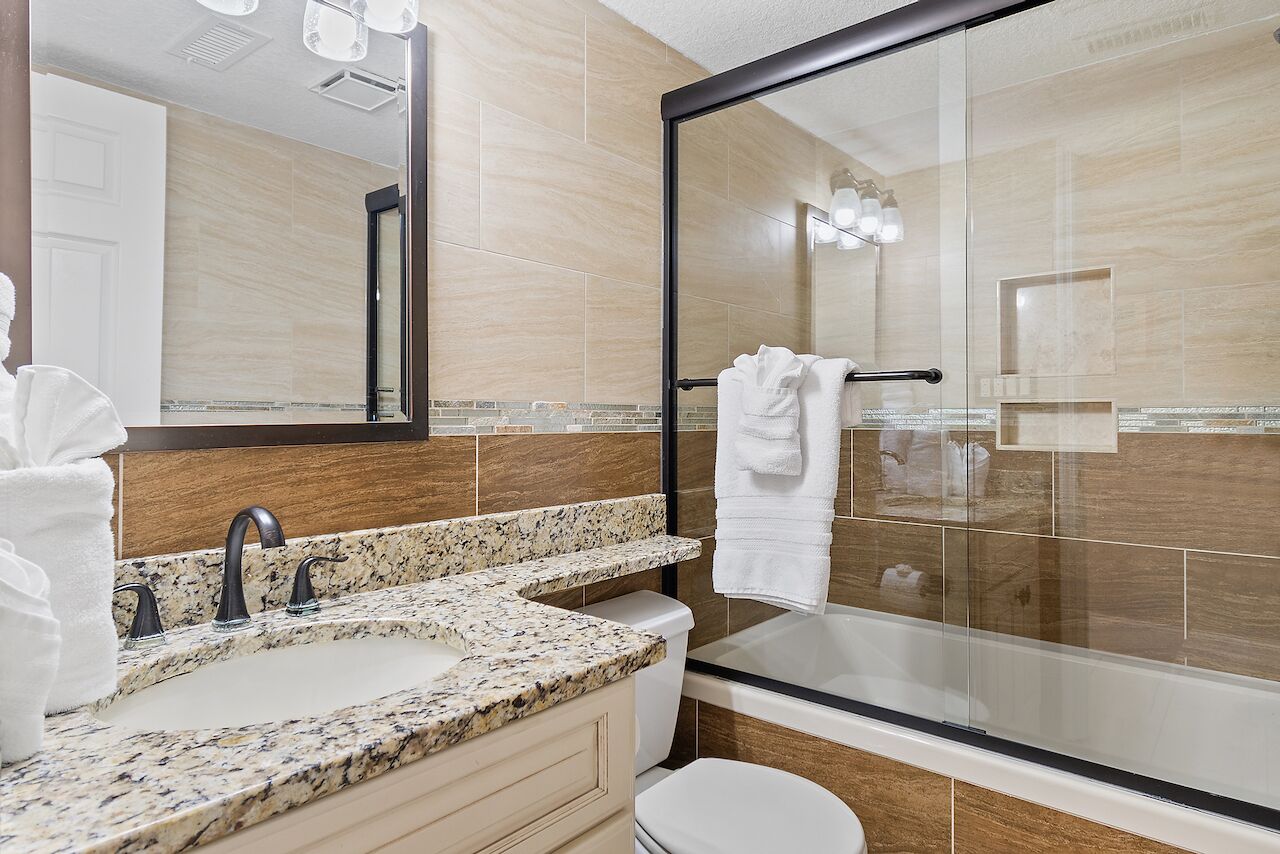 A modern bathroom with a granite countertop sink, a glass shower enclosure, and a large mirror.