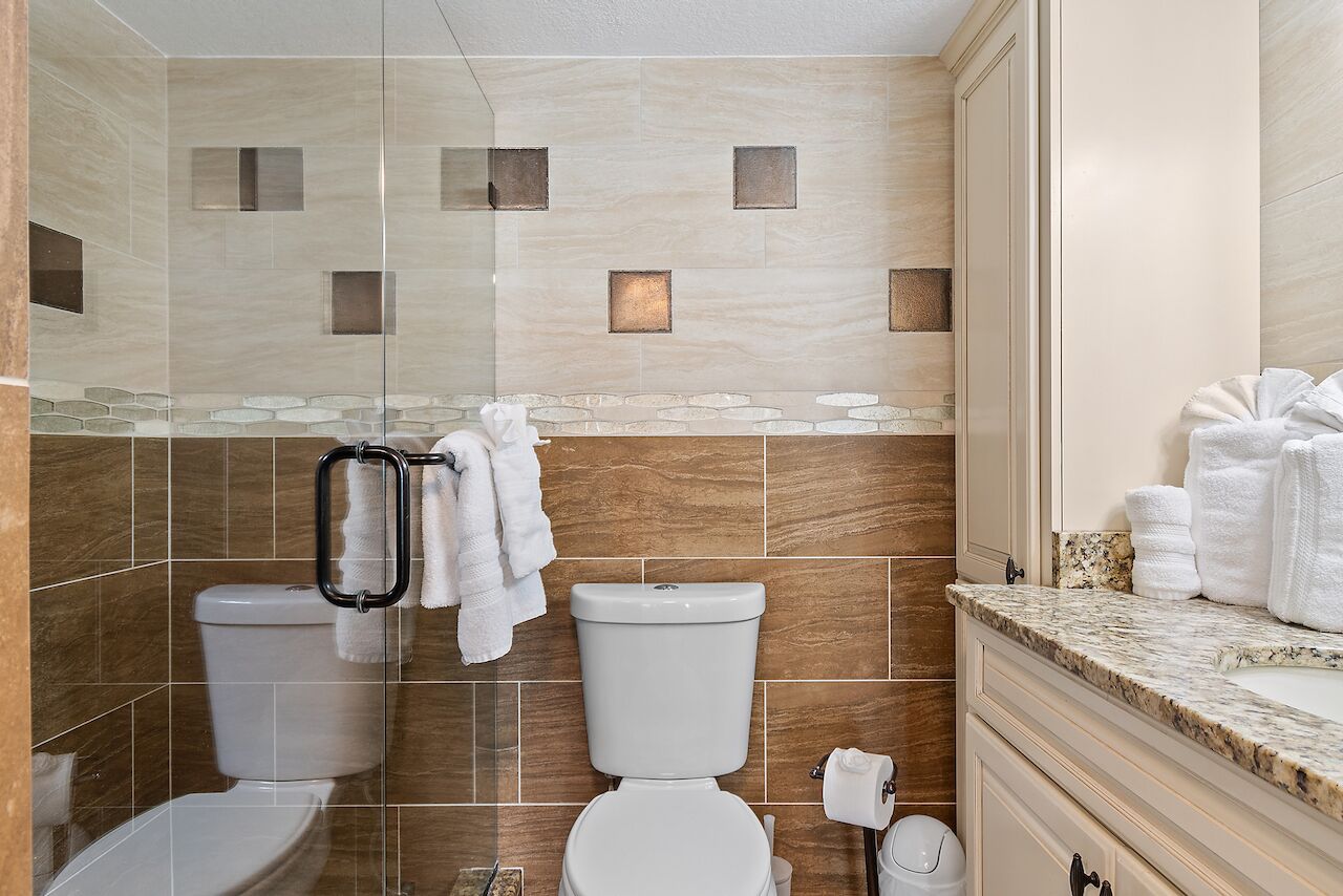 A modern bathroom with two toilets, a glass shower enclosure, and a marble countertop.