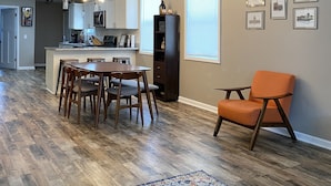 A spacious living area with a dining table, chairs, a sofa, and a kitchen in the background.