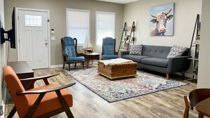 A living room with a sofa, two armchairs, a wooden chest, a rug, and a sailboat model on a side table.