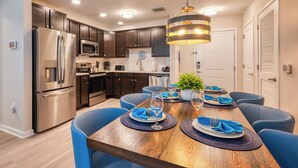 A modern kitchen with stainless steel appliances, dark wooden cabinets, and a wooden dining table set for six with blue chairs.