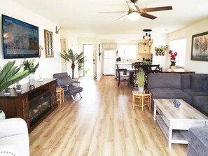 A spacious living room with a wooden floor, a gray sofa, a coffee table, and a TV mounted on the wall. - Spacious Whole Residence w/ Bikes--Close to Beach! (Oceano)
