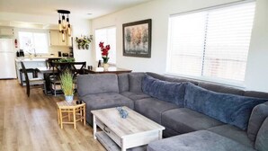 A modern living room with a grey sectional sofa, a wooden coffee table, and a dining area with a wooden table and chairs. - Spacious Whole Residence w/ Bikes--Close to Beach! (Oceano)