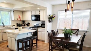 A modern kitchen with white cabinets, a central island with stools, and a dining area with a table and chairs. - Spacious Whole Residence w/ Bikes--Close to Beach! (Oceano)