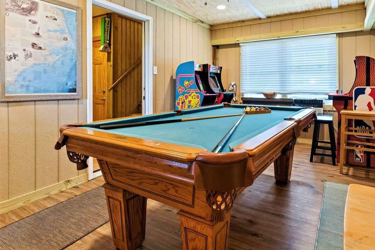 Une table de billard dans une pièce aux murs en bois, avec une porte donnant sur un autre espace.