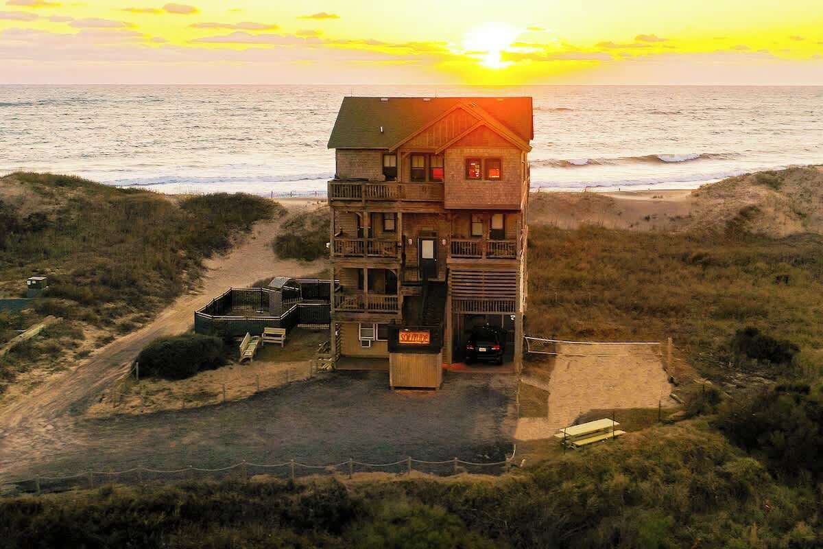 A two-story beachfront building with a balcony, a carport, and a visible entrance.