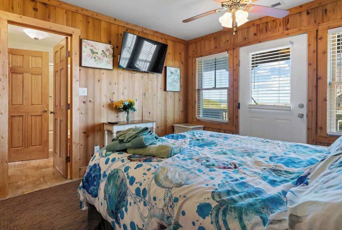 A wooden-paneled bedroom with a bed, a television, and a door.