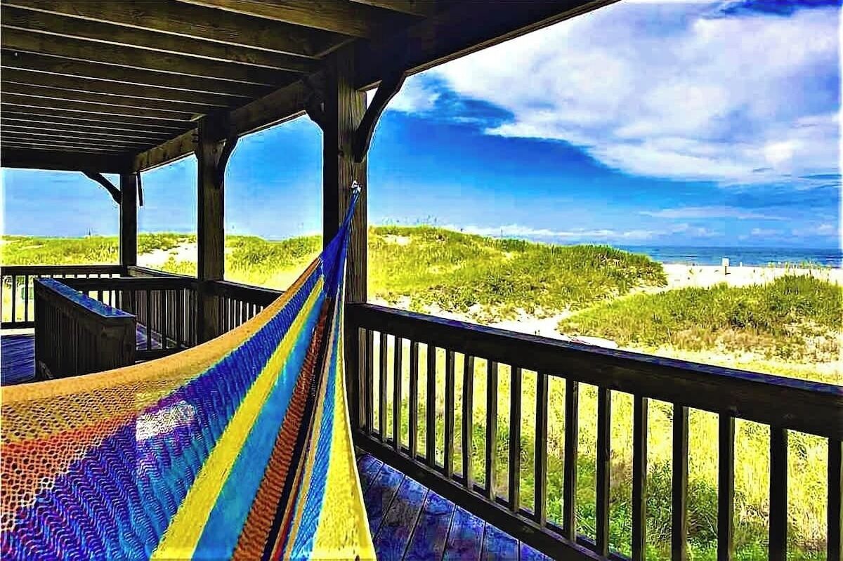 A wooden deck with a hammock overlooking a beach and dunes.