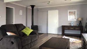 Ein Wohnzimmer mit einem dunkelgrauen Sofa, einem Holztisch, einem Kamin und einem Schreibtisch mit Lampe.