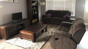 Ein Wohnzimmer mit einer dunkelholz-Multimediamöbel, einem Flachbildfernseher, einem braunen Ledersofa und einem großen Fenster mit Jalousien.