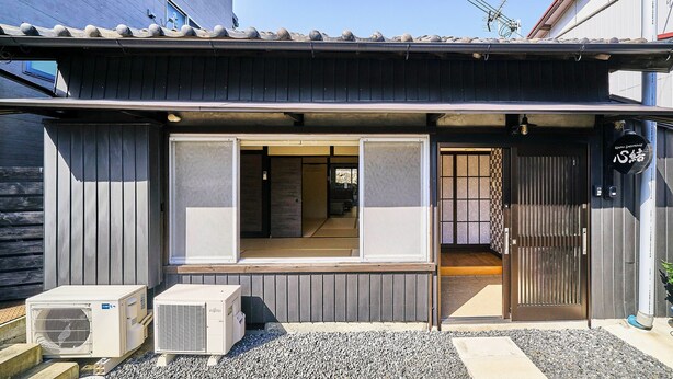 A traditional Japanese building with a sliding door, air conditioning units, and a small outdoor area with gravel and potted plants.