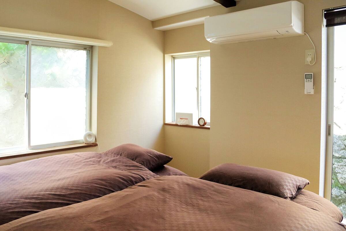 A bedroom with two beds, a window, an air conditioning unit, and a clock on the wall.