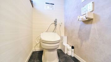 A bathroom with a toilet, a shower, and a wall-mounted electrical outlet.