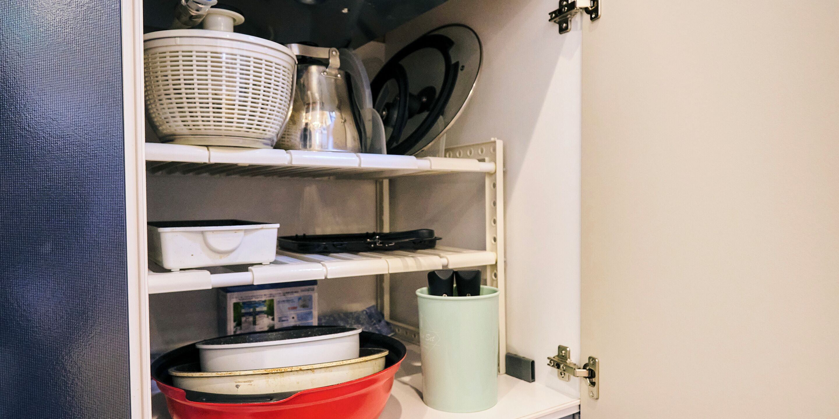 A kitchen shelf with various kitchenware including a red pot, a white bowl, and a green container.