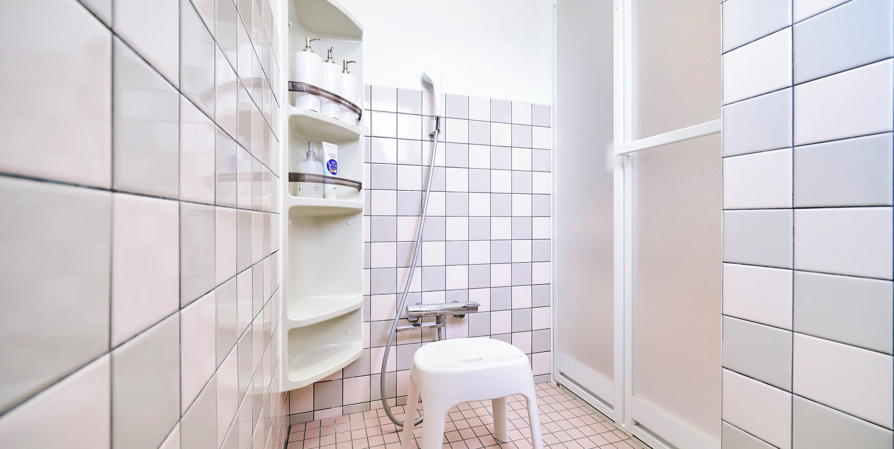 A small, tiled bathroom with a white sink, a shower, and a toilet.