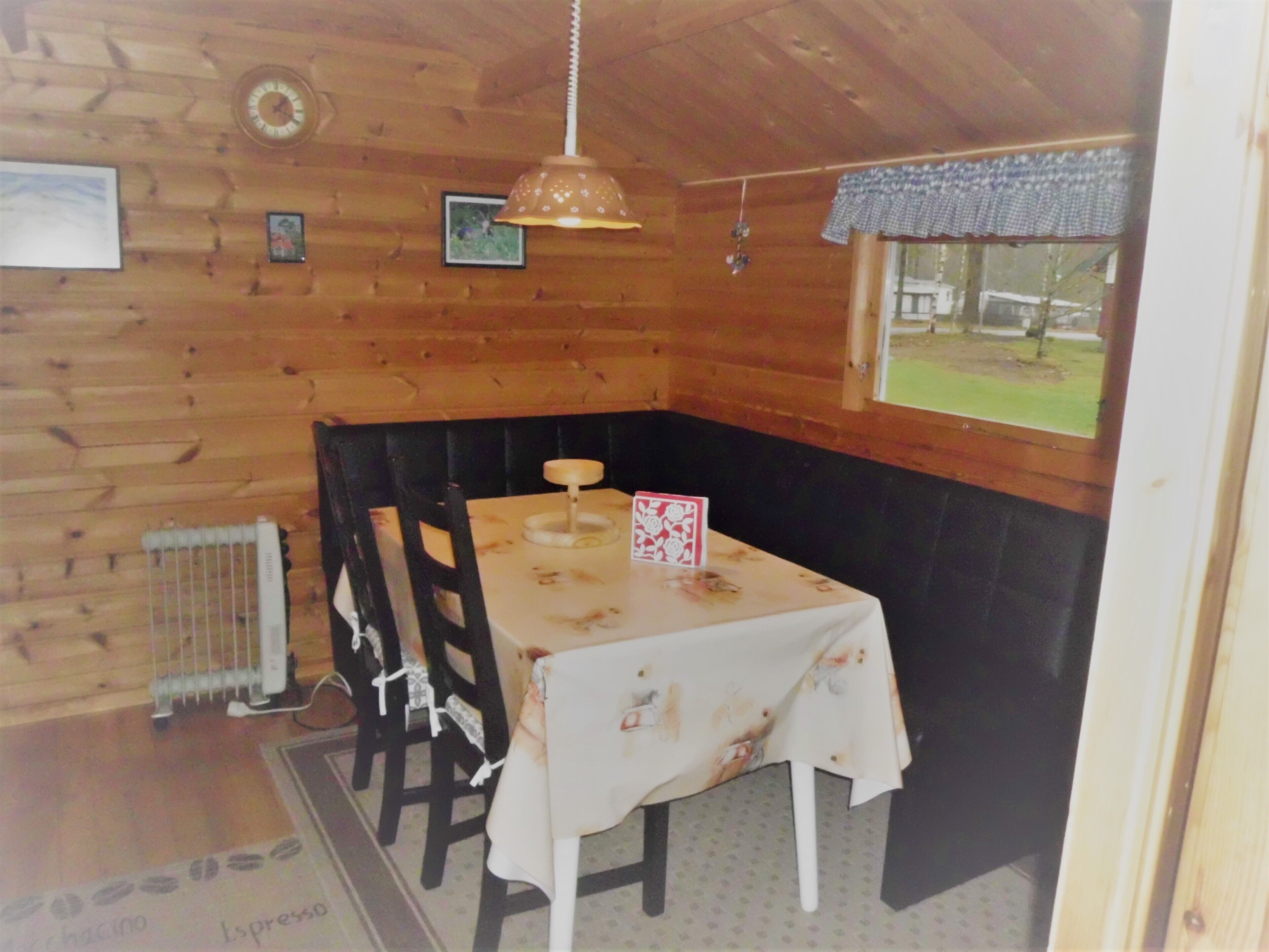 Interior de una cabaña de madera con una mesa y sillas, una lámpara colgante y una ventana que ofrece vistas al exterior.