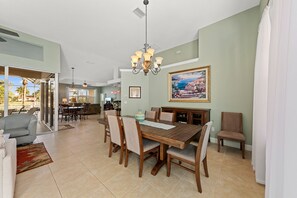 A spacious dining area with a wooden table and chairs, a chandelier, and a painting on the wall.