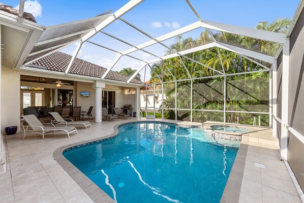 An indoor swimming pool with a glass enclosure, lounge chairs, and a bar area.