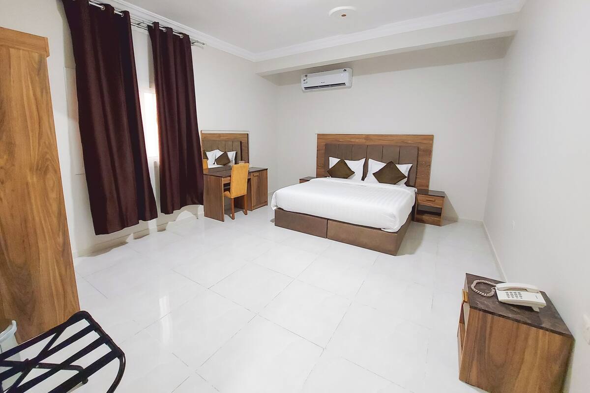 Una habitación de hotel con cama, escritorio, silla, mesita de noche, teléfono y aire acondicionado.