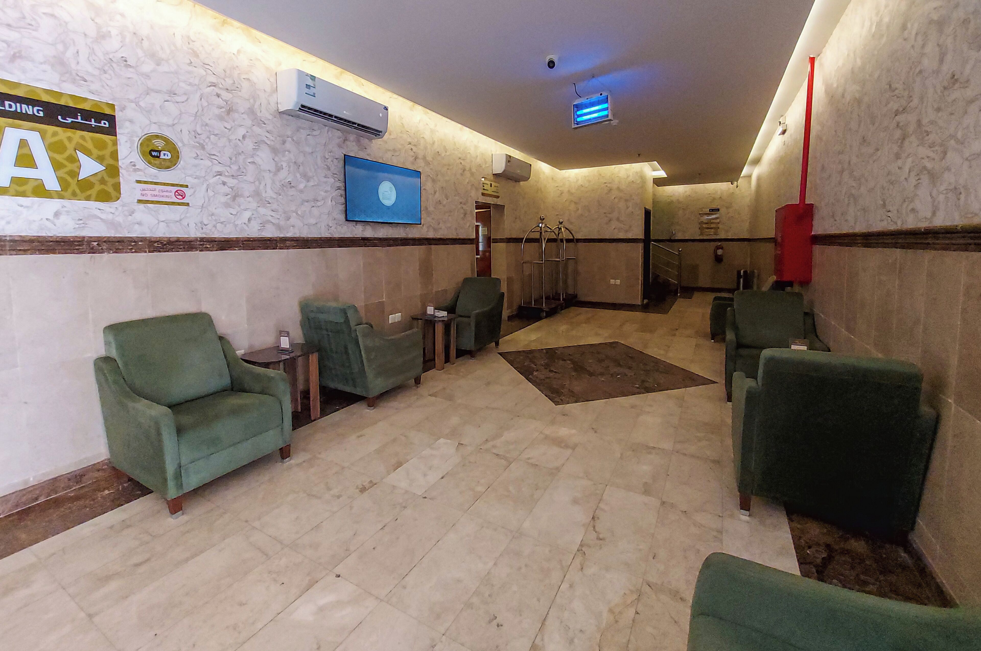 A hotel lobby with green chairs, a reception desk, and a blue sign on the wall.