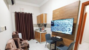Un espace de vie compact comprenant un coin cuisine, un espace salon avec un canapé et des fauteuils, et un téléviseur fixé au mur.