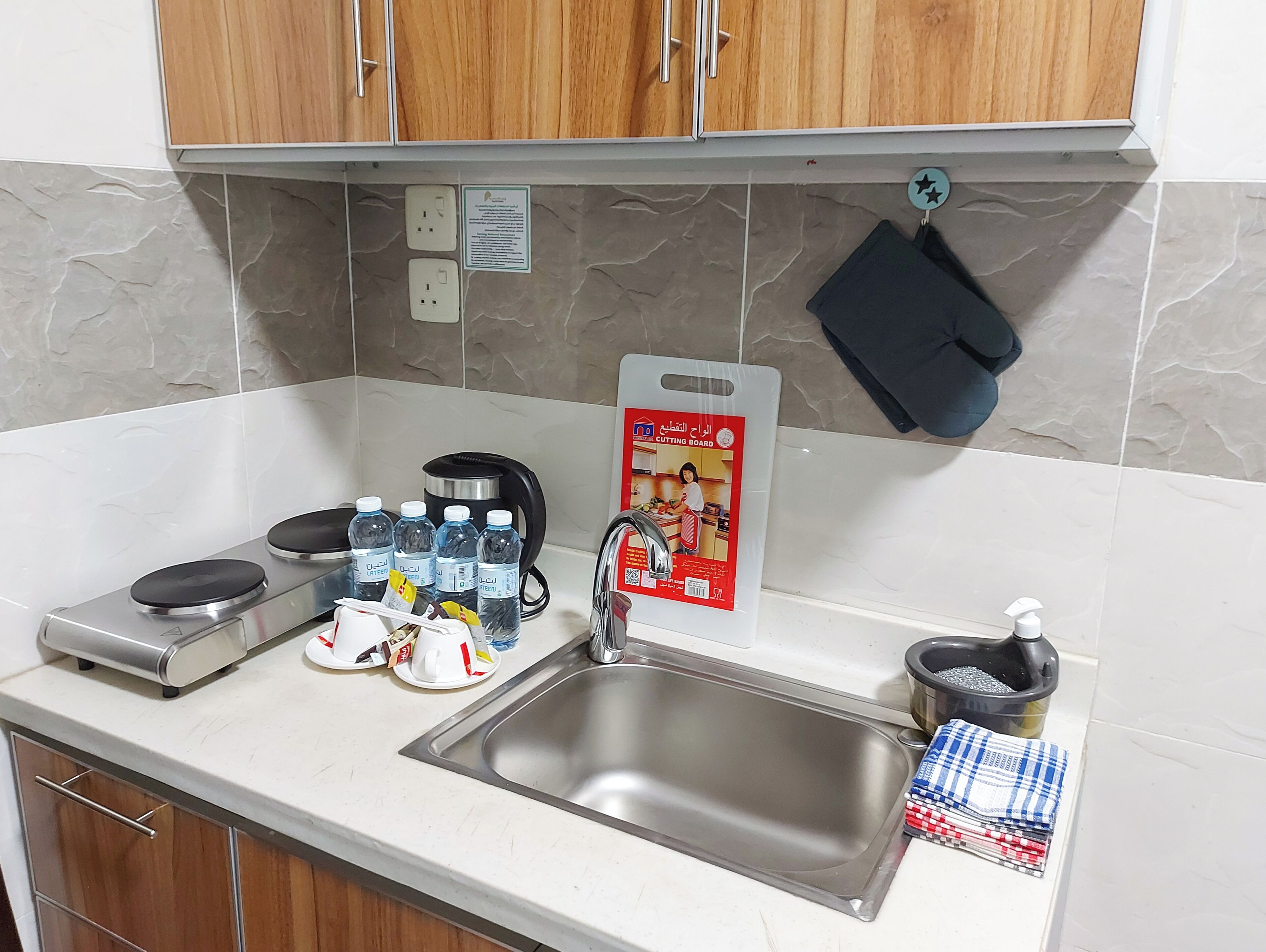 A kitchen with a stainless steel sink, a coffee maker, a cutting board, and a kettle.