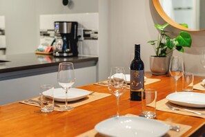 Une table à manger dressée avec des assiettes, des verres et une bouteille de vin, avec une machine à café et une plante en pot en arrière-plan.