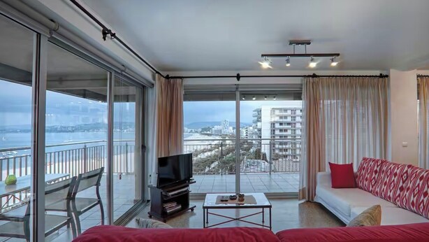 Una sala de estar moderna con un sofá rojo, un televisor y un balcón con vistas a la ciudad.