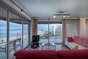 Ein modernes Wohnzimmer mit einem roten Sofa, einem Fernseher und einem Balkon mit Blick auf die Stadt.